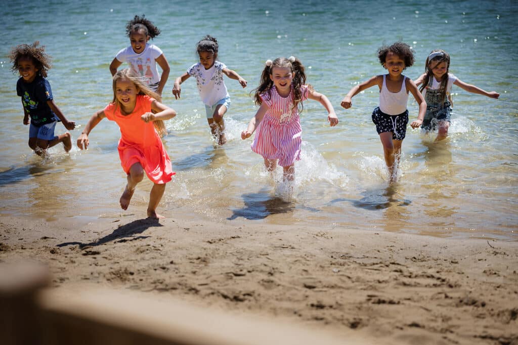 Kinderen lopen uit het water richting speeltoestellen
